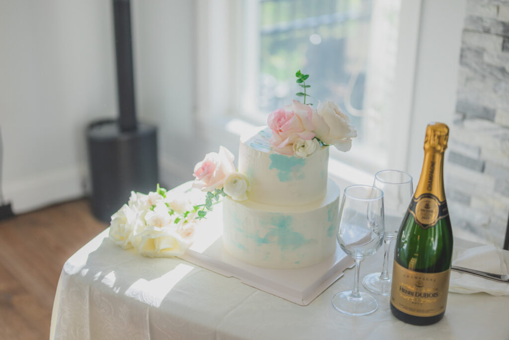 Two-tier cake adorned with pink and white roses, with champagne and flutes beside it at a party in Boston.