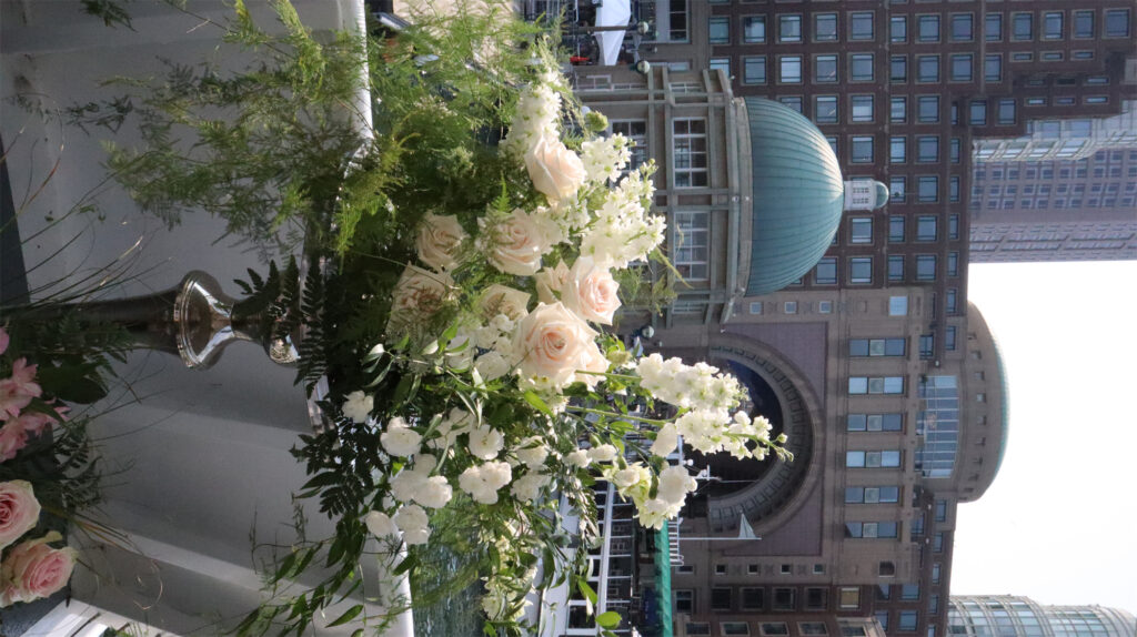 Elegant floral arrangements on a waterfront deck overlooking buildings in Boston.