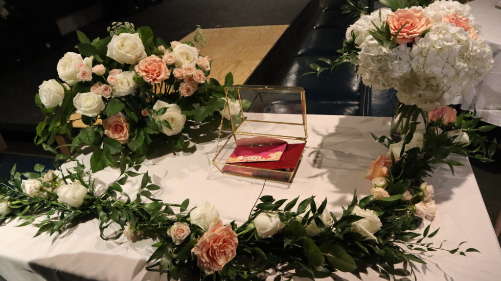 White tablecloth table with pink and white rose floral arrangements, a glass box, and greenery at a party in Boston.