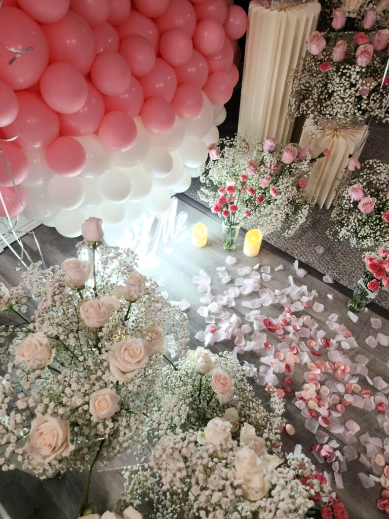 Two-tier cake adorned with pink roses and watercolor effects, alongside a champagne bottle and two glasses, at a party in Boston.