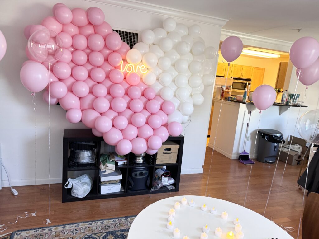 Heart-shaped balloon wall in pink and white with a "love" neon sign at a party in Boston.